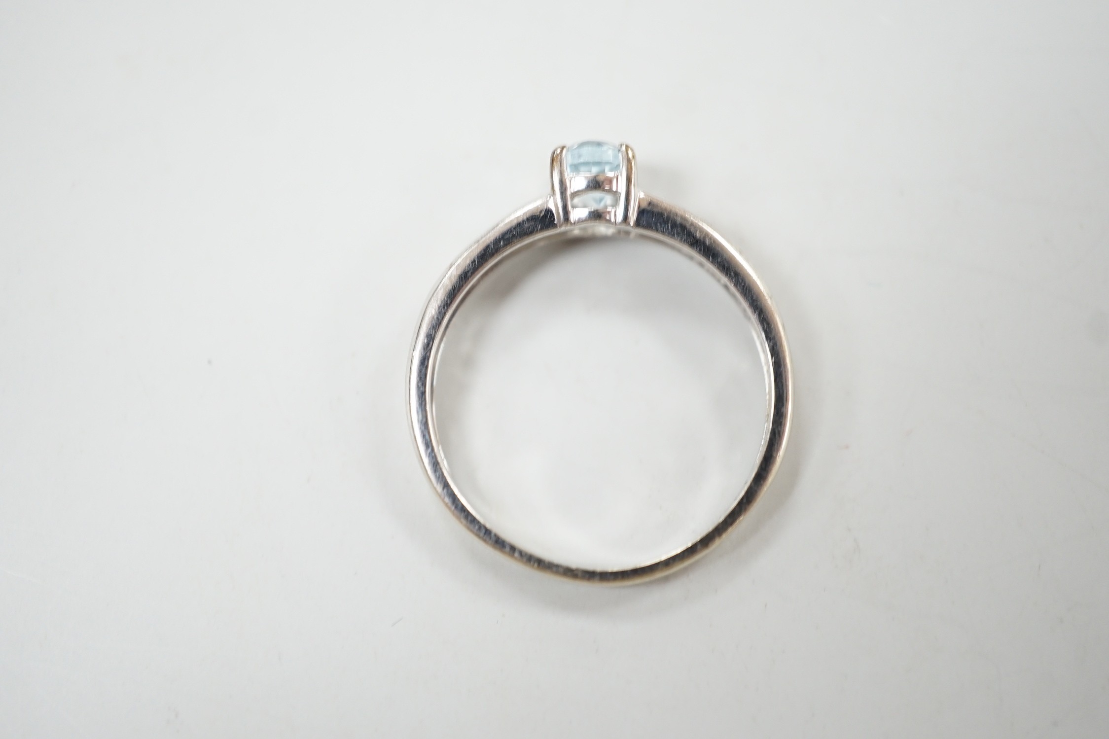A modern 9ct white gold and oval cut blue topaz ring, with diamond chip set shoulders, size N, gross weight 2 grams.